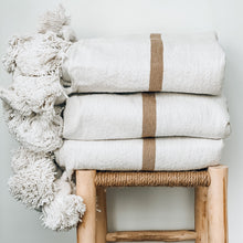 Load image into Gallery viewer, white blanket with one tan stripe with big pom pom tassels